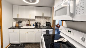 A kitchen with white cabinets, a black countertop, a stove, and a microwave.