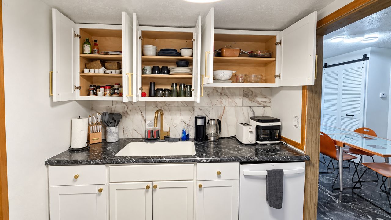 A kitchen with white cabinets, a black countertop, and a dining area with a table and chairs.