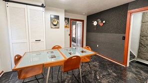 A dining area with a glass-top table, orange chairs, and a black brick wall.