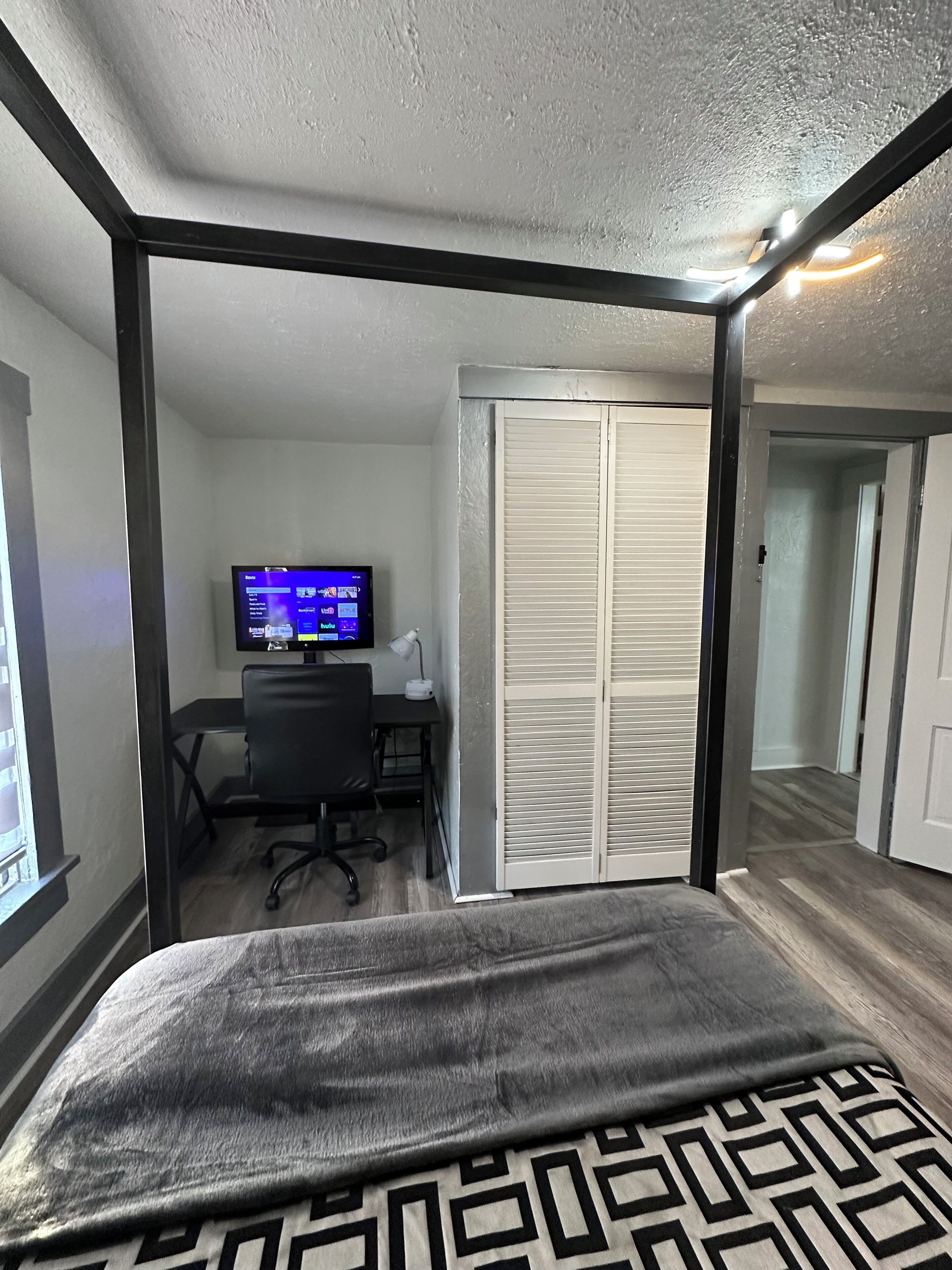 A bedroom with a bed, a desk with a computer, a TV, and a closet.