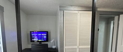 A bedroom with a bed, a desk with a computer, a TV, and a closet.