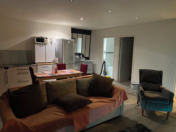 A modern living room with a sofa, a dining table, and a kitchen area in the background.
