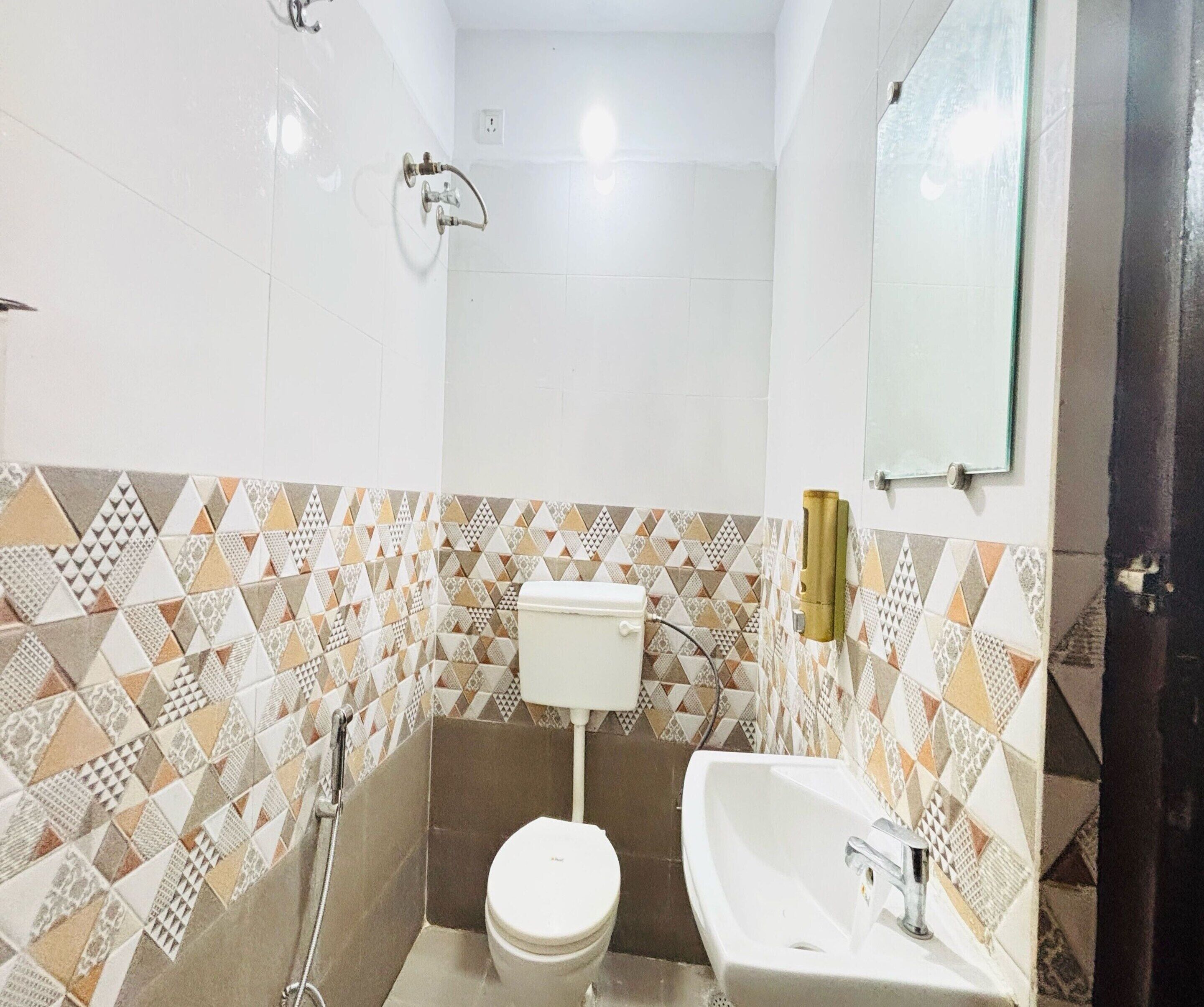 A small bathroom with a toilet, sink, and shower. The walls are tiled with a geometric pattern.