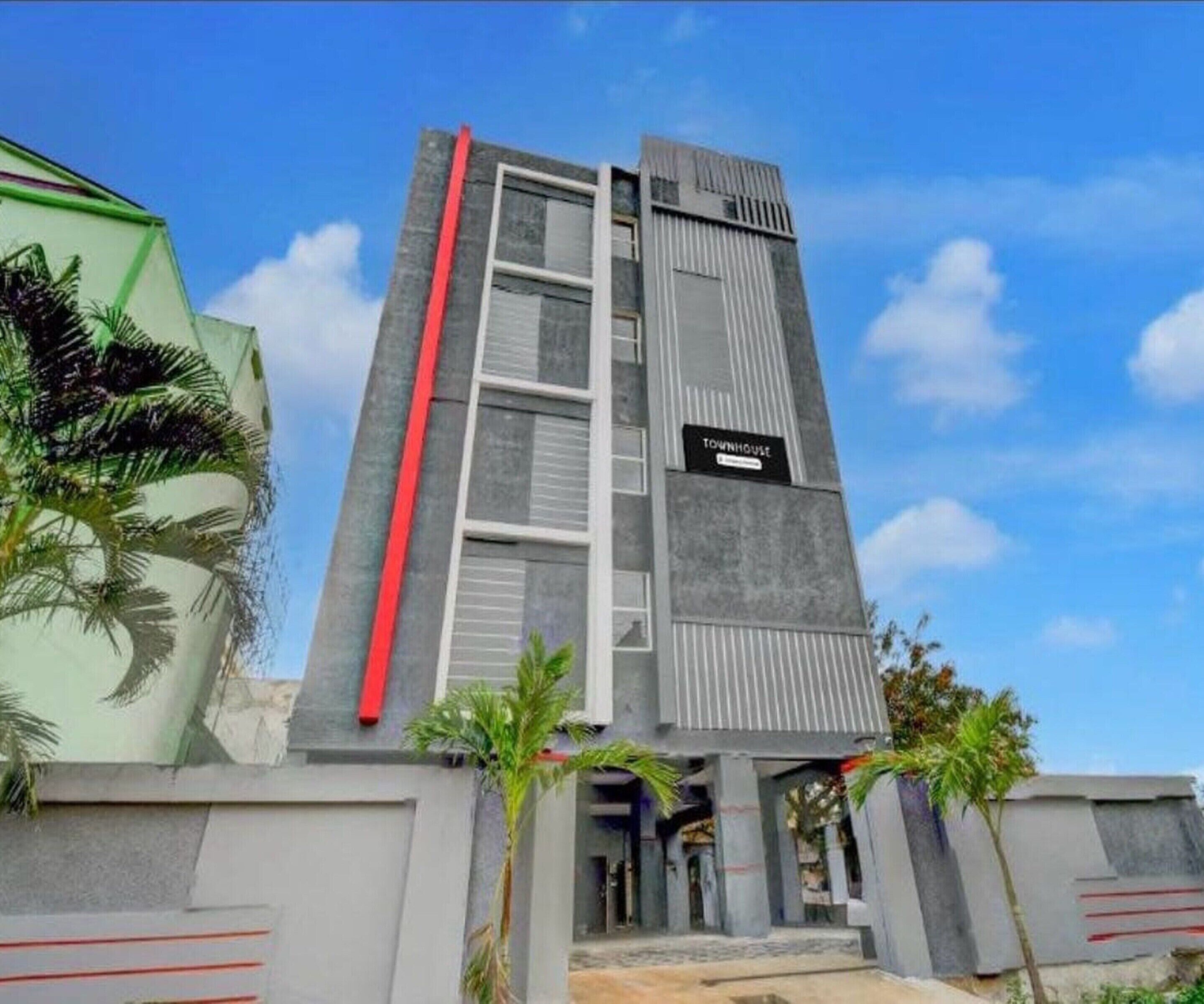 A modern building with a vertical red stripe, a sign reading "TOWNHOUSE," and a gated entrance.