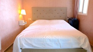 Siisti hotellihuone, jossa on huolitellusti pedattu sänky, yöpöytälamppu ja matkalaukku lattialla.