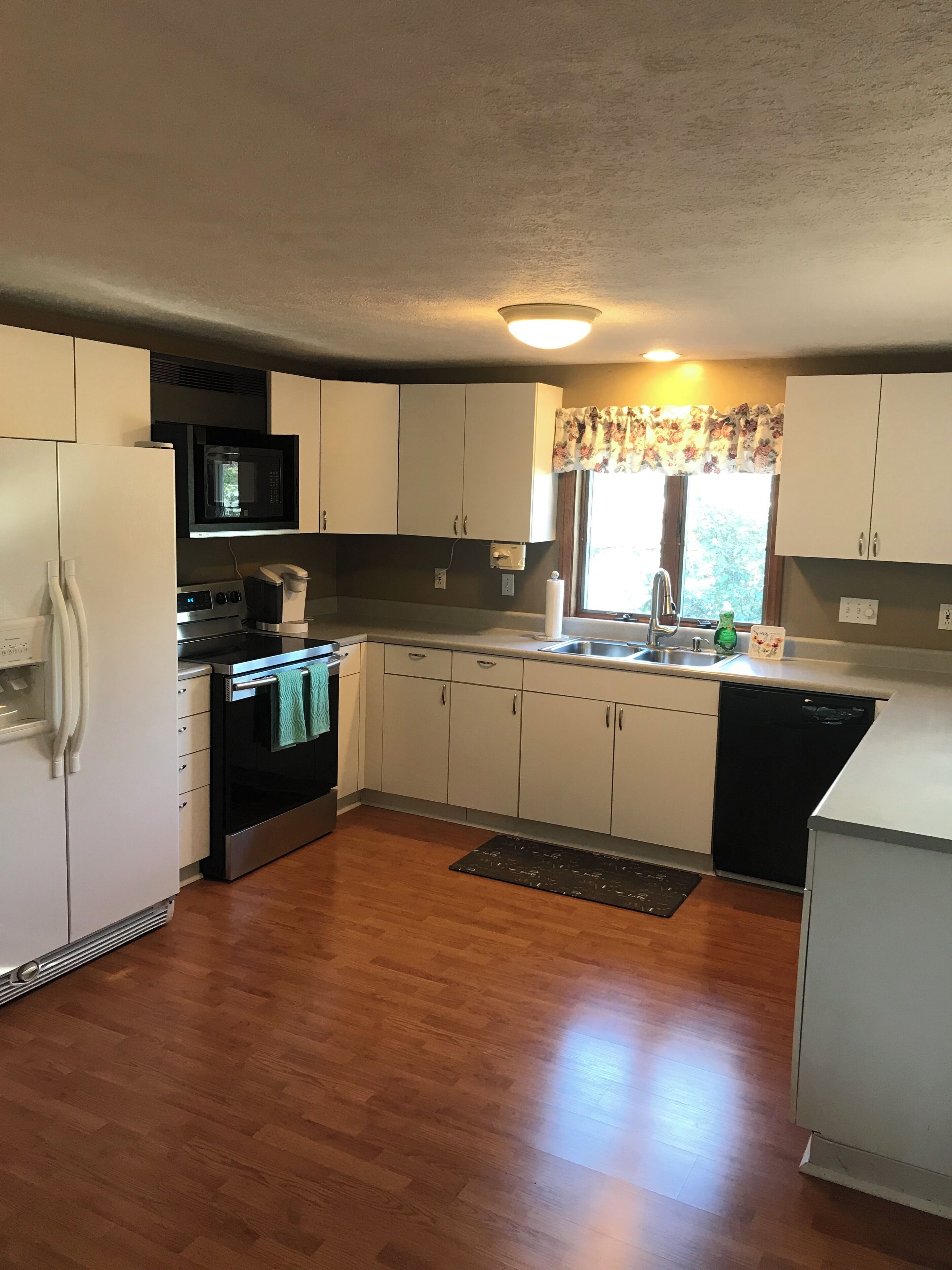 A compact kitchen with white cabinets, a microwave, an oven, a sink, and a dishwasher.