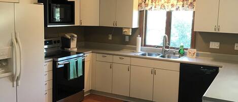 A compact kitchen with white cabinets, a microwave, an oven, a sink, and a dishwasher.