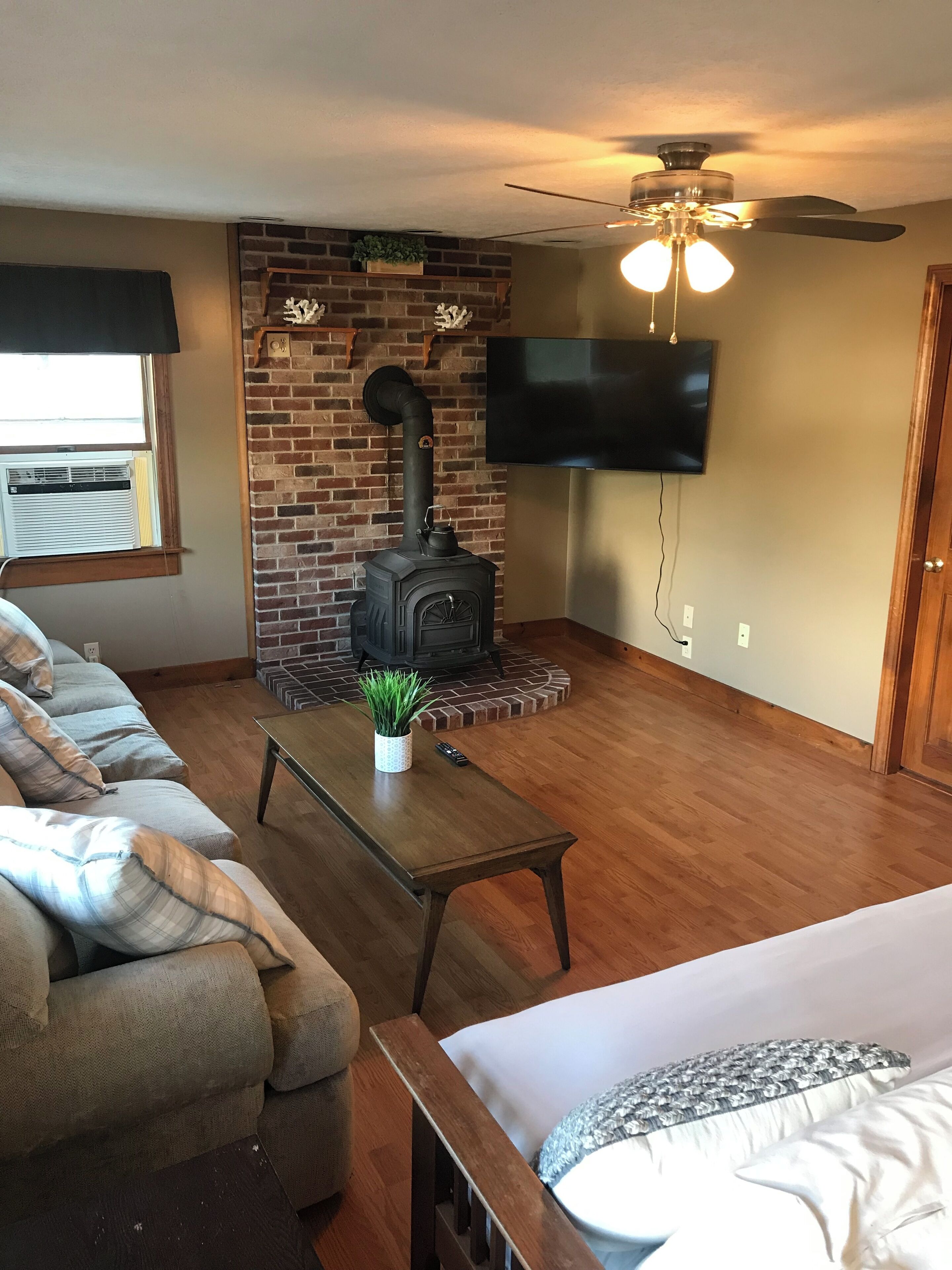 A living room with a brick fireplace, a ceiling fan, a flat-screen TV, and a sofa.