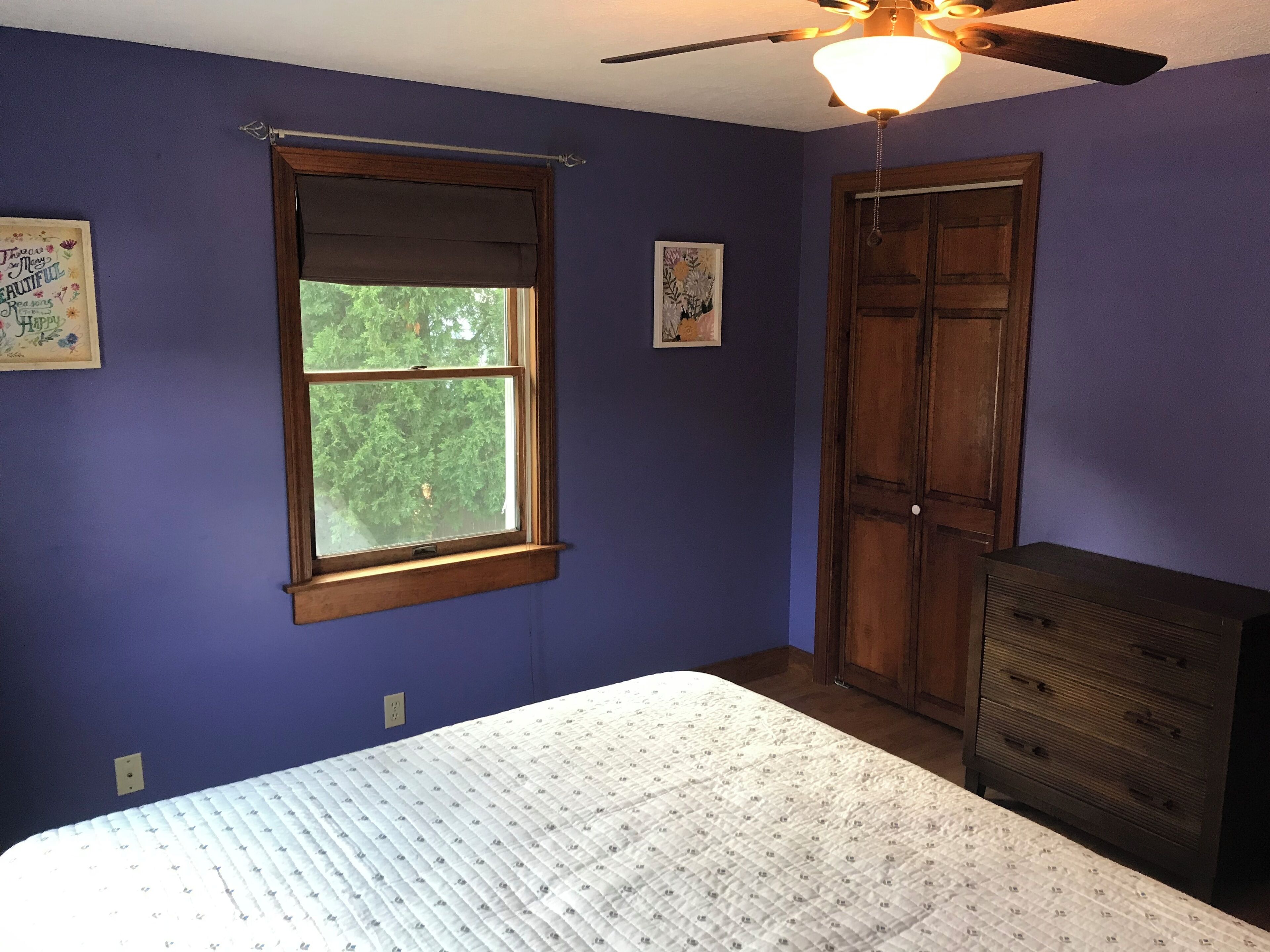 A bedroom with a bed, a dresser, a window with a view of trees, and a ceiling fan.