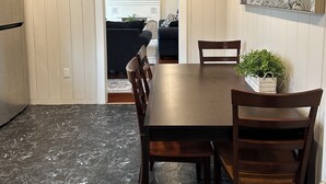 A dining area with a marble floor, wooden table, and chairs. A television is mounted on the wall, and a painting is on the wall to the right.