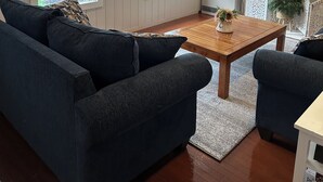 A living room with a dark blue sofa, a wooden coffee table, and a TV mounted on the wall.