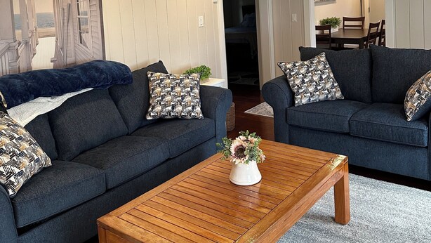 A living room with two dark blue sofas, a wooden coffee table, and a painting on the wall.