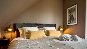 Ein ordentlich bezogenes Bett mit einem gemusterten Bettüberwurf, zwei Nachttischlampen und einem gerahmten Bild an der Wand.