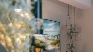 Ein modernes Wohnzimmer mit einem großen Gemälde, einem Holzkonsolentisch mit Obstschale und einer hängenden Pflanze.