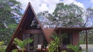 Una cabaña de madera triangular con porche cubierto y dos sillas.