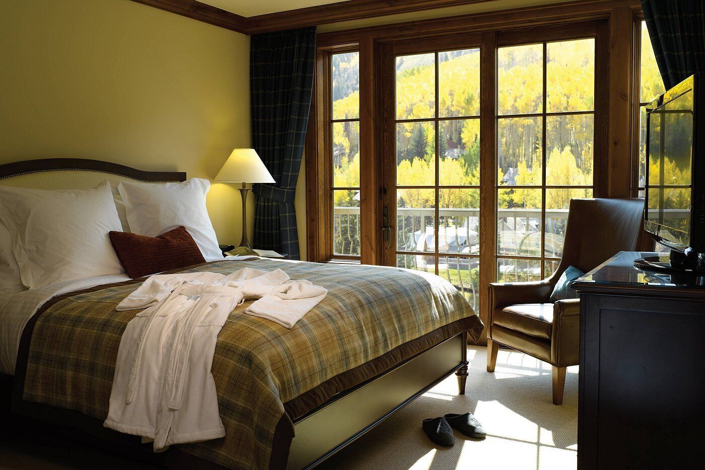 A hotel room with a large bed, a desk, and a view of a forest through a large window.
