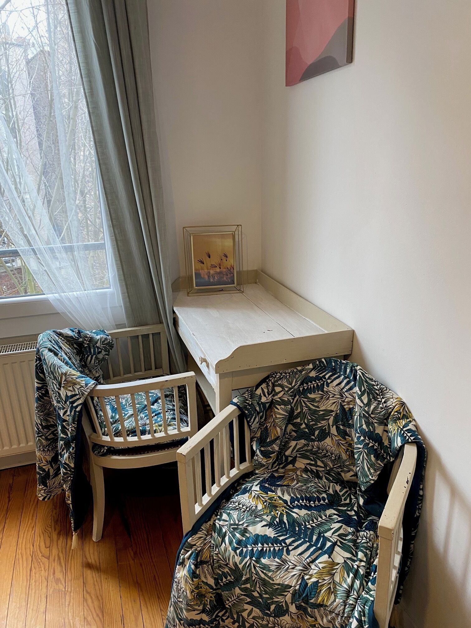 A room with a crib, a chair, a table, and a window with curtains.