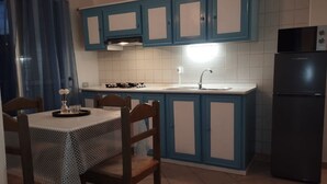 Ett kök med blå skåp, ett svart kylskåp, en diskho och ett matbord med stolar.