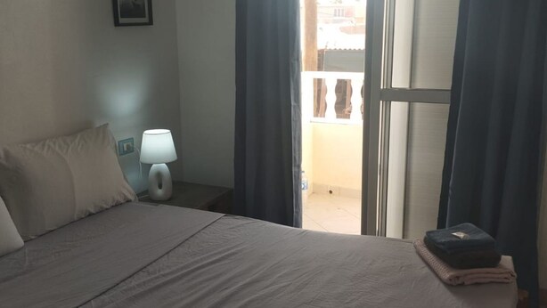 Ett hotellrum med en säng, ett nattduksbord med en lampa och utsikt över balkongen.