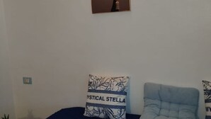 Ett rum med en blå soffa, en väggmonterad ljusströmbrytare och en inramad tavla ovanför soffan.