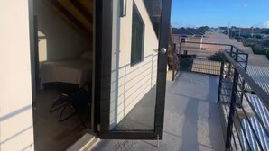Un balcón con puerta de cristal que da a una habitación con cama y sillón.