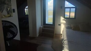 Un dormitorio con cama, ventana y puerta que da a una escalera.