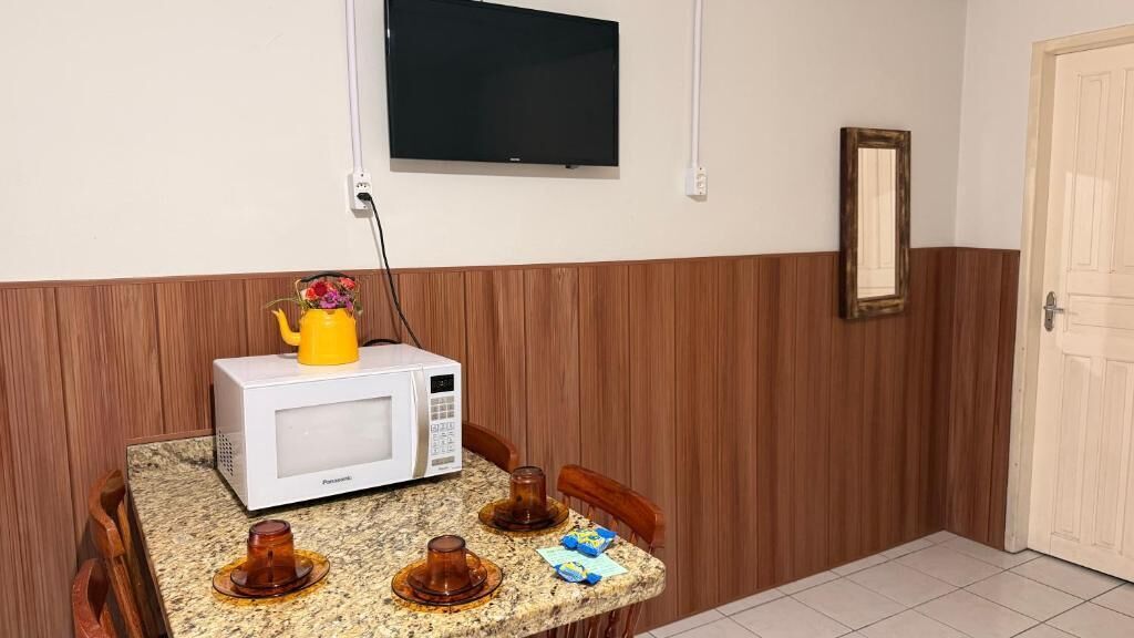 Una cocina con microondas, una mesa pequeña y un televisor montado en la pared.