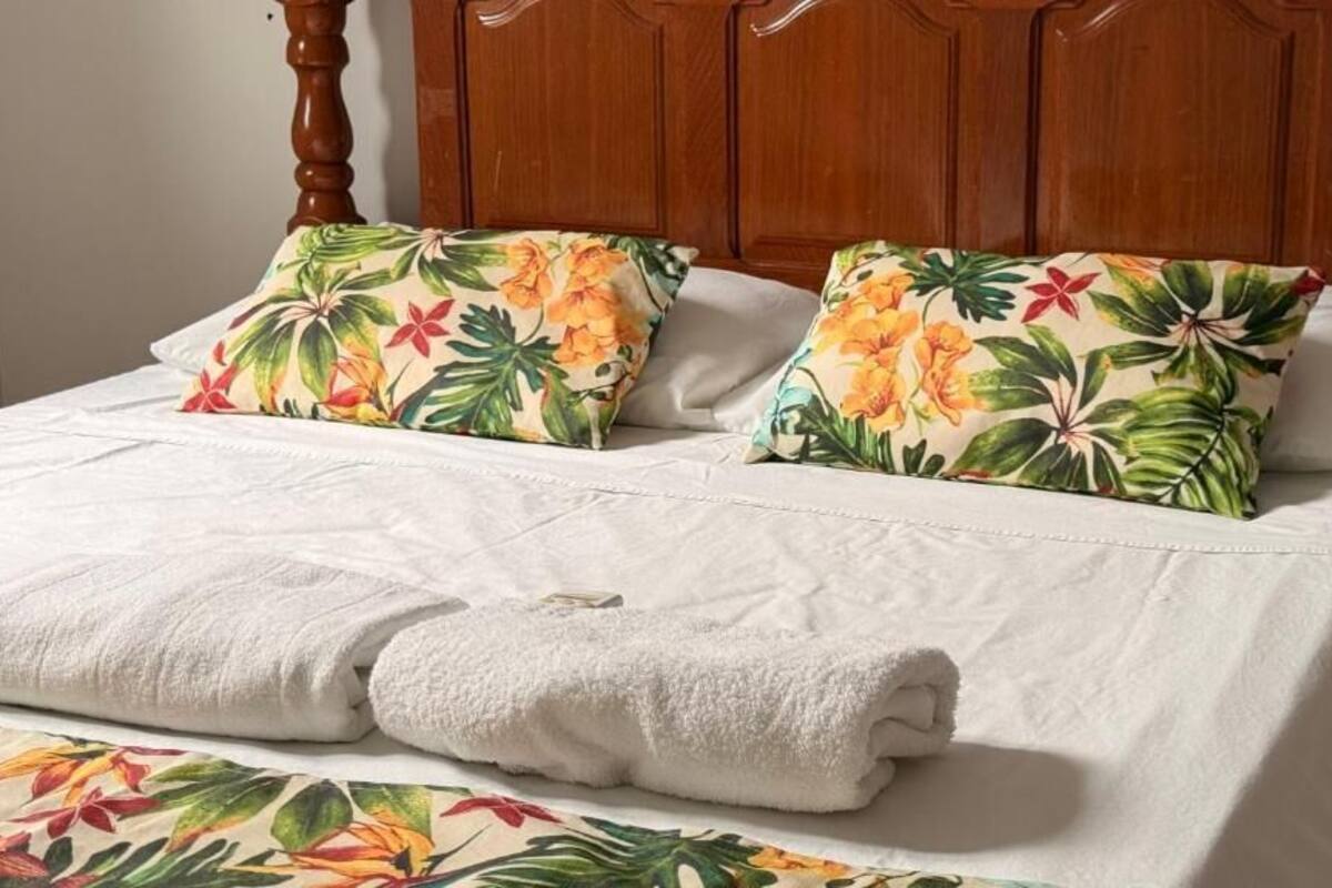 Un lit bien fait, agrémenté d’oreillers à motifs floraux et d’une serviette blanche.