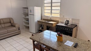 A compact kitchen with a refrigerator, stove, and a small sink. There is a beige sofa and a dining table with chairs.
