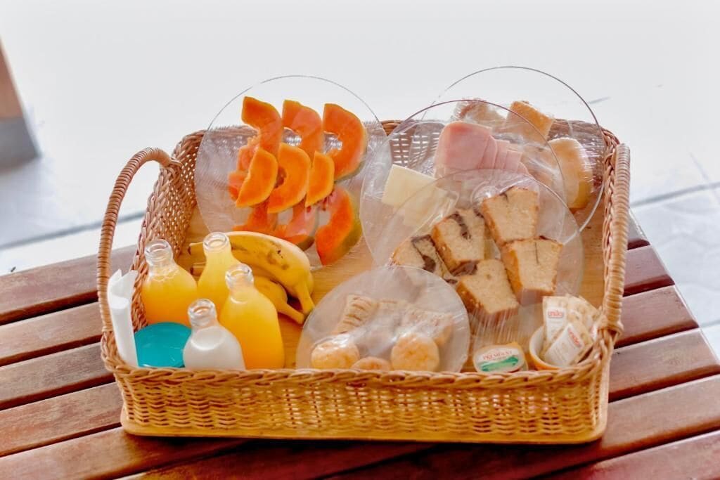 Una cesta de mimbre con diferentes alimentos, como rodajas de naranja, plátanos, pan y aperitivos envasados.