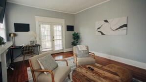 A living room with two armchairs, a coffee table, a TV, and a painting on the wall. - Modern One bedroom near downtown and Augusta National (Augusta)