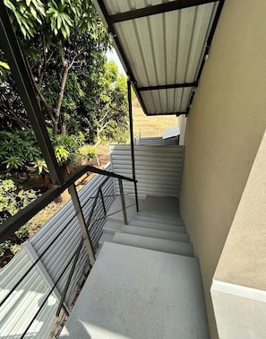 Una escalera de hormigón con barandillas de metal que conduce a un espacio cubierto con techo de láminas metálicas.