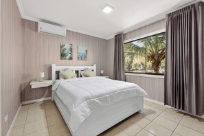 A bedroom with a bed, nightstands, a window with curtains, and a wall-mounted air conditioner. - Modern Condo w / Pool in Playa Coco (Coco)