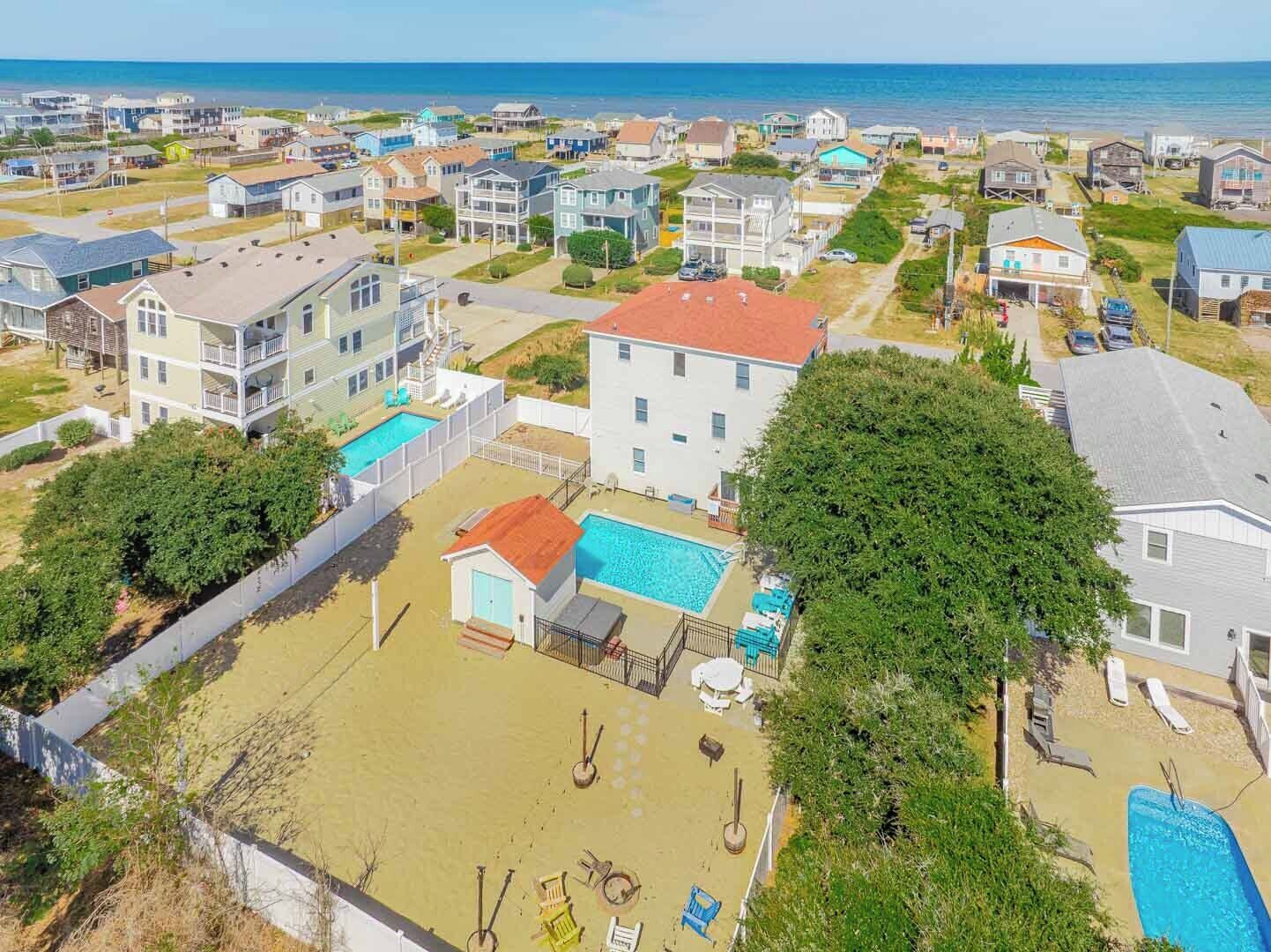 A residential area with houses, a swimming pool, and a beach in the background.