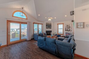 Ein geräumiges Wohnzimmer mit Kamin, einer großen Couch und Blick auf den Strand durch Glastüren.