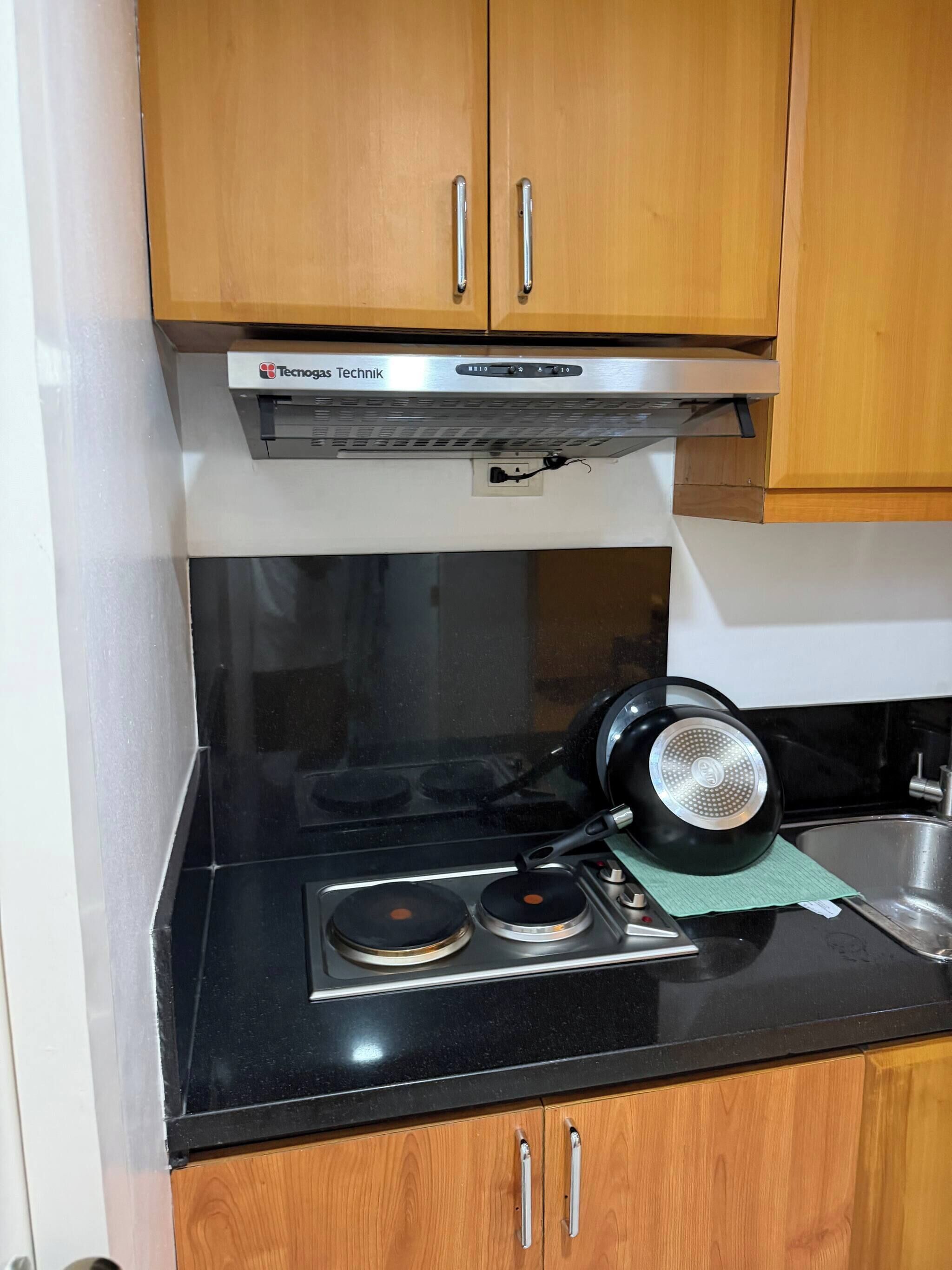 A kitchen with a stove, a black pot, and wooden cabinets.