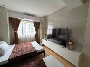 Habitación de hotel con dos camas, televisor y ventana con cortinas.