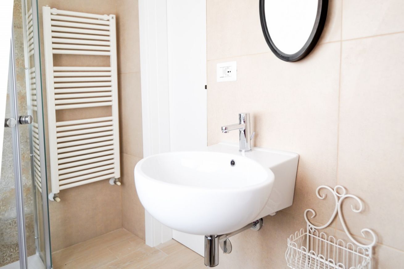 Een badkamer met een witte wastafel, een spiegel, een handdoekhouder en een douche.