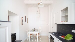 A compact kitchen with white cabinetry, a dining table with chairs, a black countertop, and a hanging light fixture. - Casa Santa Pietra, charming flat in Pietrasanta's center (Pietrasanta)