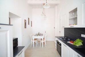 A compact kitchen with white cabinetry, a dining table with chairs, a black countertop, and a hanging light fixture. - Casa Santa Pietra, charming flat in Pietrasanta's center (Pietrasanta)