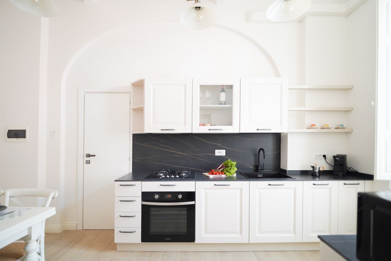 A modern kitchen with white cabinetry, a black marble countertop, and a built-in oven.