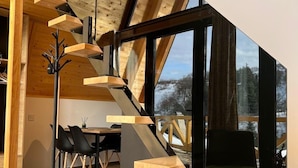 A modern interior with a wooden staircase, a dining area, and large windows offering a view of the outdoors. - A frame cabins in the heart of a national park! (Rakovac)