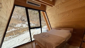 A cozy bedroom with a large window, wooden walls, and a bed with a white blanket. - A frame cabins in the heart of a national park! (Rakovac)
