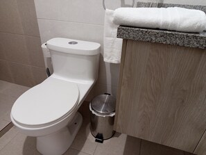 A white toilet with a closed lid, a trash bin, and a towel hanging on a towel rack. - Comfortable apartment for 8 people, North of Quito, close to Solca and US embassy. (Quito)