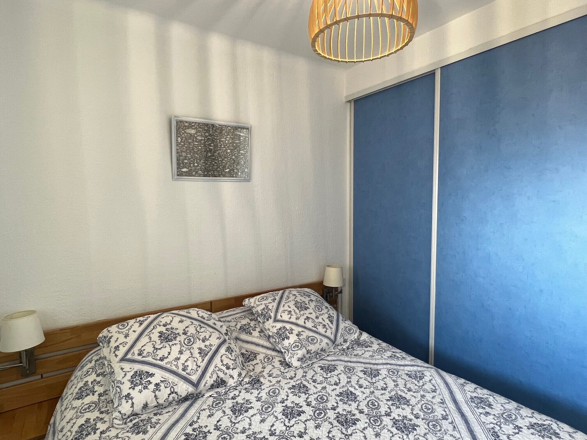 Un dormitorio con una cama, una lámpara de noche, un cuadro en la pared y una pared decorada en azul.