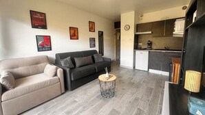 Een woonkamer met een bank, een salontafel en een keukenhoek met kastjes en een spoelbak.