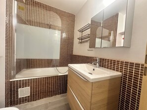 A bathroom with a bathtub, a sink, and a mirror. - Les Terrasses de l'Espiguette - studio rénové terrasse plage à pied (Le Grau-du-Roi)