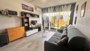 Een moderne woonkamer met een grijze bank, een houten dressoir, een tv-meubel en een groot raam met gordijnen.