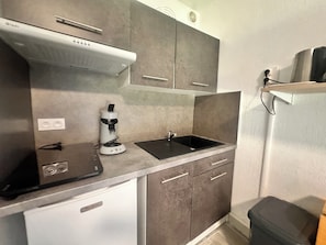Een kleine keuken met een ingebouwde magnetron, een koffiezetapparaat, een spoelbak en een prullenbak.