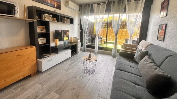 Een moderne woonkamer met een grijze bank, een houten dressoir en een televisie op een zwart voetstuk.